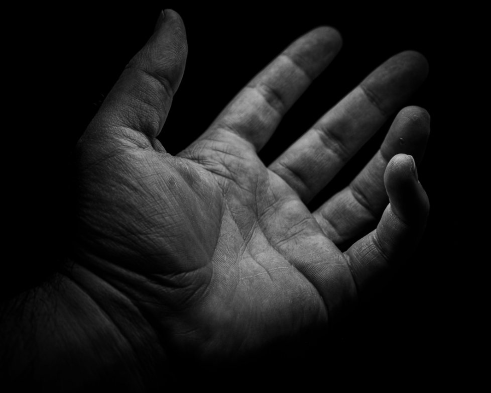 Grayscale shot of a human hand reaching out toward an unknown entity against a black background. demonic encounters